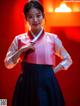 A woman in a pink and black hanbok poses for a picture.