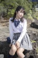 A woman in a school uniform sitting on a rock.