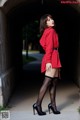 A woman in a red coat and black stockings posing for a picture.