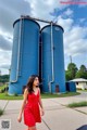 A woman in a red dress standing in front of two blue silos.